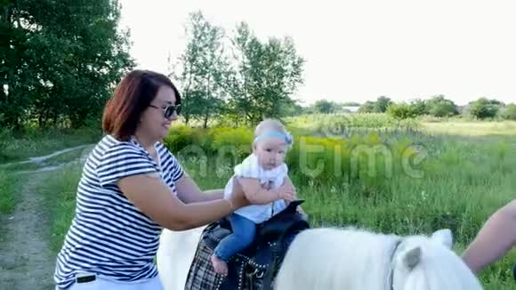 一个带着孩子的女人在田野里走来走去一个婴儿坐在小马上妈妈抱着孩子快乐的家庭假期视频的预览图