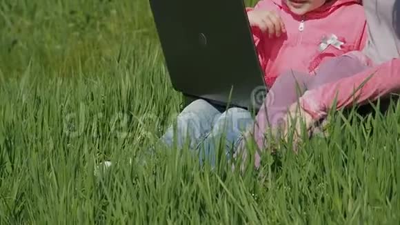 公园里有两个小女孩带着笔记本电脑的女人在阳光明媚的日子里幸福的家庭妈妈和女儿在草地上视频的预览图