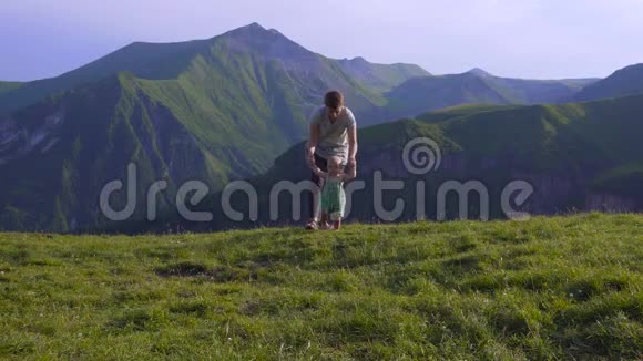 年轻的母亲带着小男孩在悬崖上放松欣赏山谷景色山区假日视频的预览图