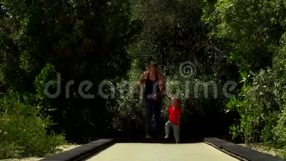 有趣的小男孩和妈妈一起在公园的蹦床跑道上奔跑和跳跃视频的预览图