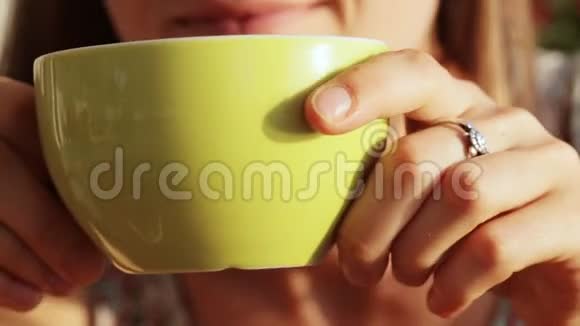 年轻漂亮的女人端着茶或咖啡坐着大口大口地喝着视频的预览图