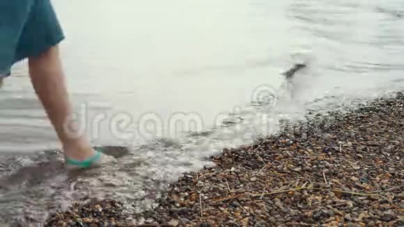 一个女人穿着凉鞋走在鹅卵石海岸视频的预览图