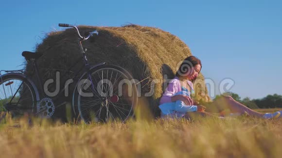 母亲和女儿在阳光明媚的日子里在一片干草堆的田野里家庭妈妈和快乐的女儿他们骑自行车进来视频的预览图