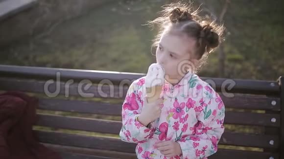 小女孩在公园长凳上吃舔冰淇淋筒视频的预览图