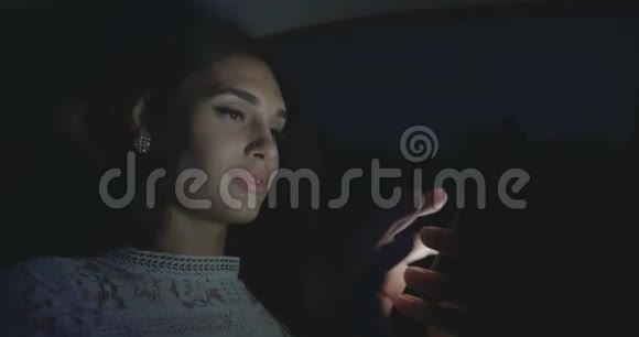 漂亮的女人晚上坐在车里用智能手机视频的预览图
