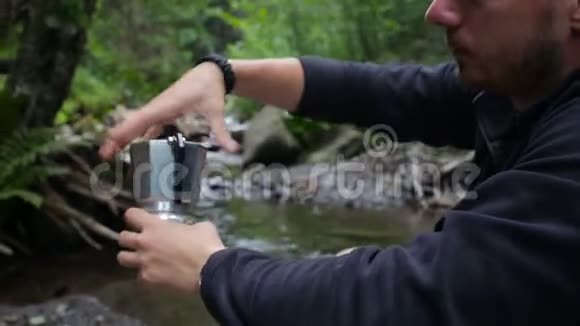 在河岸的一个露营地一个游客把水倒进咖啡机里视频的预览图