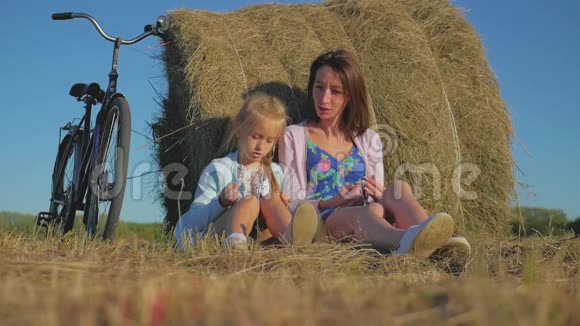 母亲和女儿在阳光明媚的日子里在一片干草堆的田野里家庭妈妈和快乐的女儿他们骑自行车进来视频的预览图
