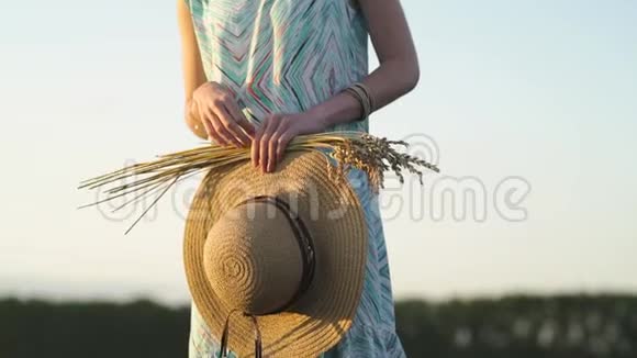 戴太阳镜的女孩站在日落时的田野里拿着金色的麦穗和草帽乡村户外场景视频的预览图