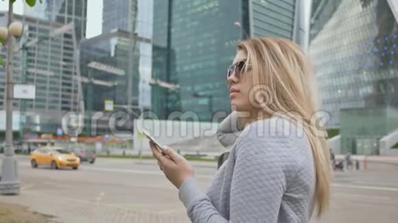 美丽的金发女郎戴着太阳镜在市中心的背景下使用手机视频的预览图