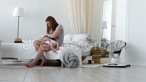 年轻的母亲抱着她新生的孩子妈妈在照顾宝宝女人和新出生的男孩在白色的卧室里放松母亲视频的预览图
