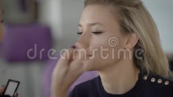 一张年轻女孩脸的近照在专业刷子海绵的帮助下将化妆涂在脸上视频的预览图