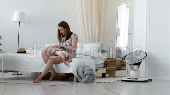 年轻的母亲抱着她新生的孩子妈妈在照顾宝宝女人和新出生的男孩在白色的卧室里放松母亲视频的预览图