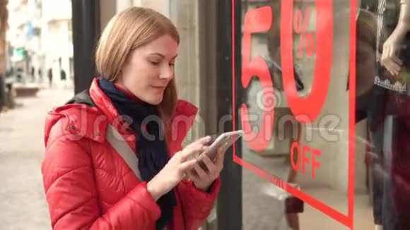 窗店附近美丽迷人的年轻女子销售标志通过智能手机读取QR码视频的预览图