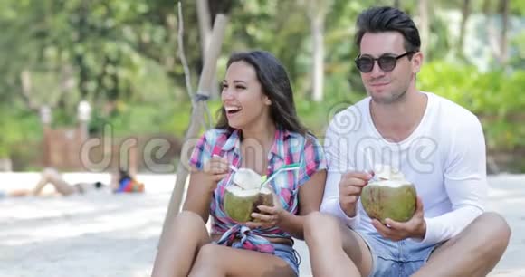 沙滩上的情侣饮料椰子鸡尾酒棕榈树下的谈话欢乐的男人和女人的游客交流视频的预览图