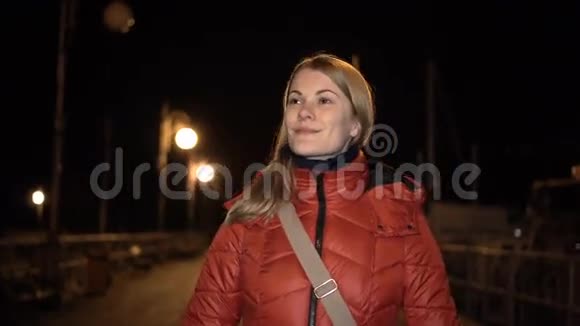 美丽迷人的年轻女子穿着红色外套走在码头上微笑夜夜黑暗视频的预览图