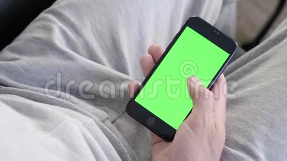 男人在家坐在沙发上使用带有绿色模拟屏幕的智能手机视频的预览图