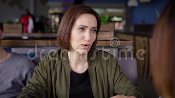 靠近一个年轻漂亮的女人坐在餐馆里花时间在她的朋友的社会里可爱视频的预览图