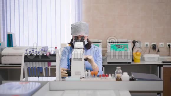 女研究助理穿蓝色擦洗戴防护面罩戴帽子和手套坐在实验室检查医疗视频的预览图