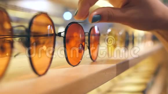 女性顾客在购物中心货架上选择带有橙色镜片的太阳镜4K动作缓慢视频的预览图