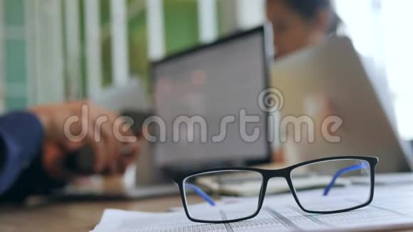 年轻的程序员戴上眼镜开始使用电脑笔记本电脑办公室的桌子上放着眼镜4K视频的预览图