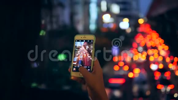 年轻的旅游女孩用手机拍摄曼谷城市的夜晚汽车交通泰国4K视频的预览图