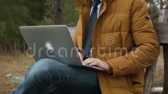 领带男商人在秋天的树木背景下在公园的长凳上使用笔记本电脑在露天工作视频的预览图