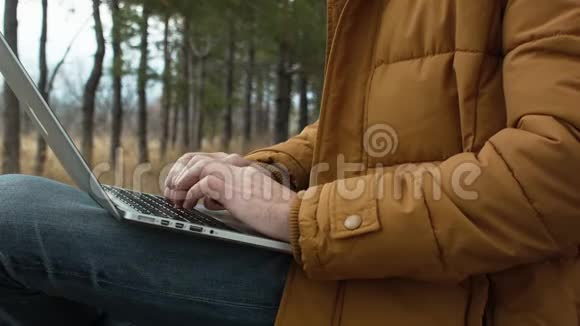 一个商人喜欢在公园里树背景的长凳上放笔记本电脑视频的预览图