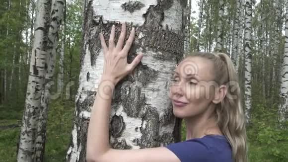 一位年轻女子的肖像她有一头白桦树的长发她拥抱着白桦树的树干视频的预览图