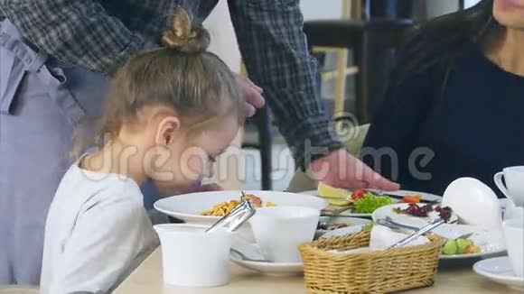 可爱的小女孩在意大利餐馆的意大利面条里倒奶酪而她的年轻父母却吃他们的蔬菜视频的预览图