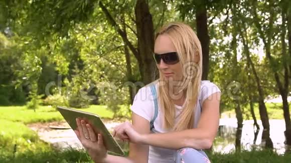 年轻女子坐在公园里拿着平板电脑慢动作视频的预览图