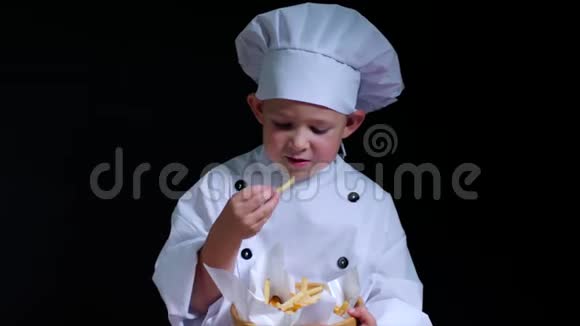 穿着厨师服的聪明男孩在黑色背景下吃炸薯条视频的预览图