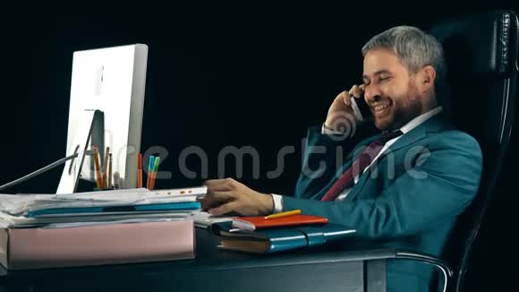 长胡子的商人在电脑上工作在手机上聊天黑色背景4K视频视频的预览图