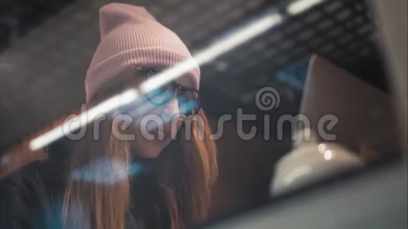 一个穿眼镜的时髦女孩在咖啡馆里的笔记本电脑上打字从窗口看到底部视频的预览图