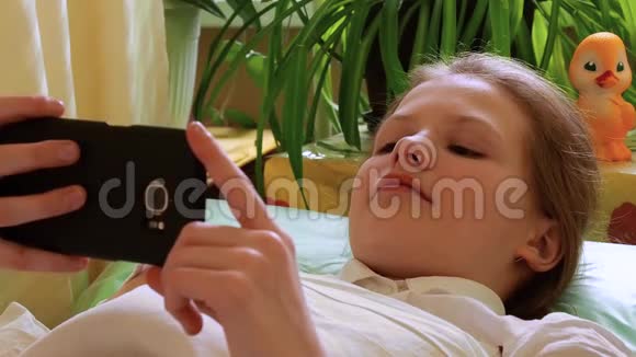 躺在医院沙发上的女孩在智能手机上覆盖着毯子手表视频视频的预览图