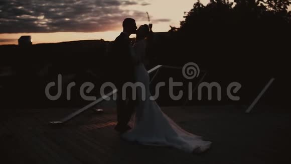 新婚夫妇在夕阳下拥抱亲吻的剪影视频的预览图