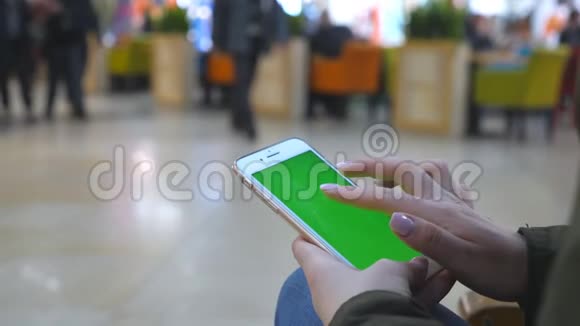 女性手使用现代智能手机与绿色屏幕年轻女孩坐在商场的长椅上轻敲视频的预览图