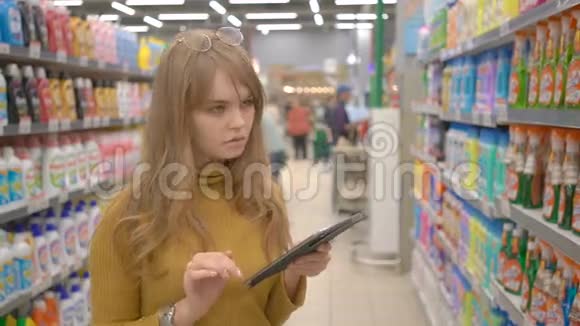 年轻漂亮的女孩在超市购物在平板电脑上寻找有关产品的信息视频的预览图