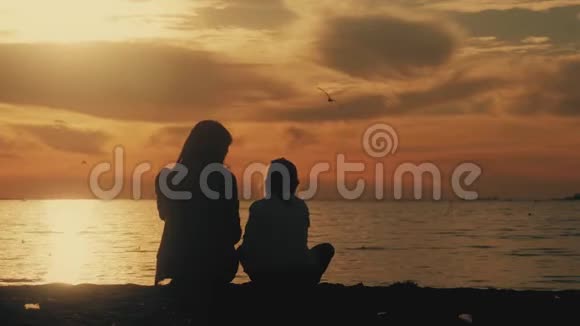 日落时分母亲和女儿坐在海滩上友好家庭观念生活方式视频的预览图