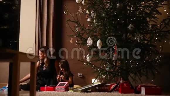 妈妈和她的女儿在他们家客厅的树下释放圣诞礼物丝带视频的预览图