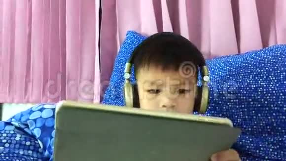 亚洲孩子戴着耳机在平板电脑上看卡通视频的预览图