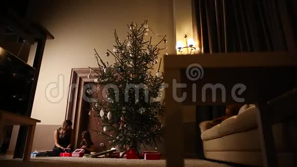 妈妈和她的女儿在他们家客厅的树下释放圣诞礼物丝带视频的预览图