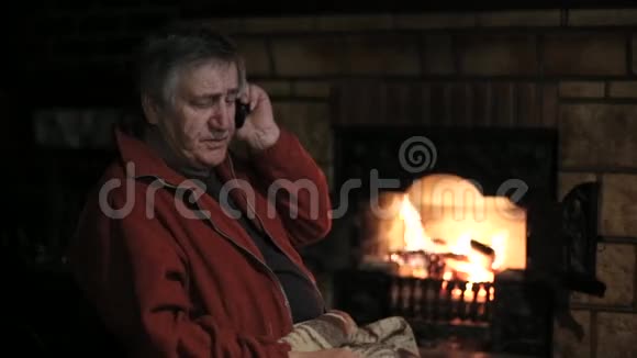 坐在壁炉前的椅子上用手机说话的老人视频的预览图