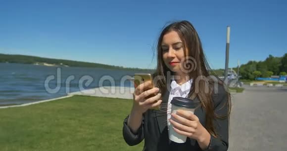 女人浏览手机在公园散步散步时喝咖啡视频的预览图