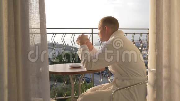 一个穿着白色长袍的年轻人在露台上喝咖啡4K视频的预览图