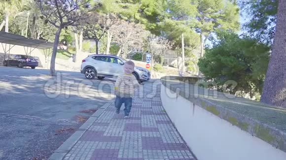 阳光明媚的夏天stadicam拍摄的小男孩在人行道上奔跑慢动作视频的预览图