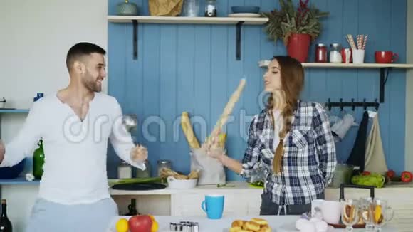 快乐的一对夫妇在厨房里玩在家里做早餐时用勺子和擀面杖打架视频的预览图