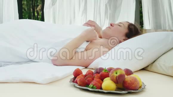 一个年轻的女人在一个休息室醒来窗帘覆盖着在她附近有一盘水果华丽的浪漫假期视频的预览图