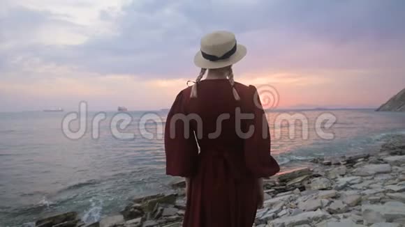 从后面看到的慢动作画一个穿着红色裙子的小女孩和一顶草帽在海滨与一个视频的预览图