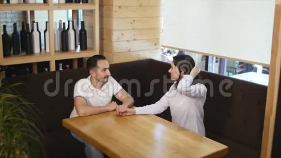一对幸福的年轻夫妇双手牵手看着对方坐在咖啡馆里微笑着视频的预览图