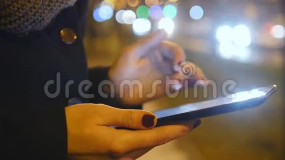 年轻女孩晚上在城市户外使用平板电脑美丽模糊的夜晚城市交通背景关门视频的预览图